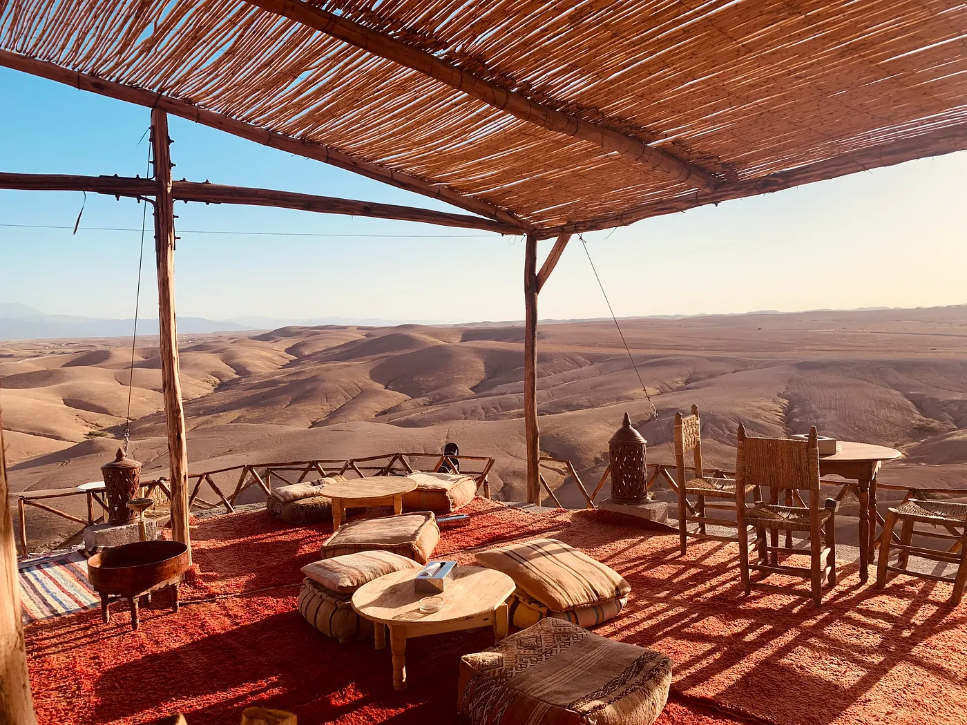 A shaded terrace with rugs and low tables looking out over the Moroccan desert