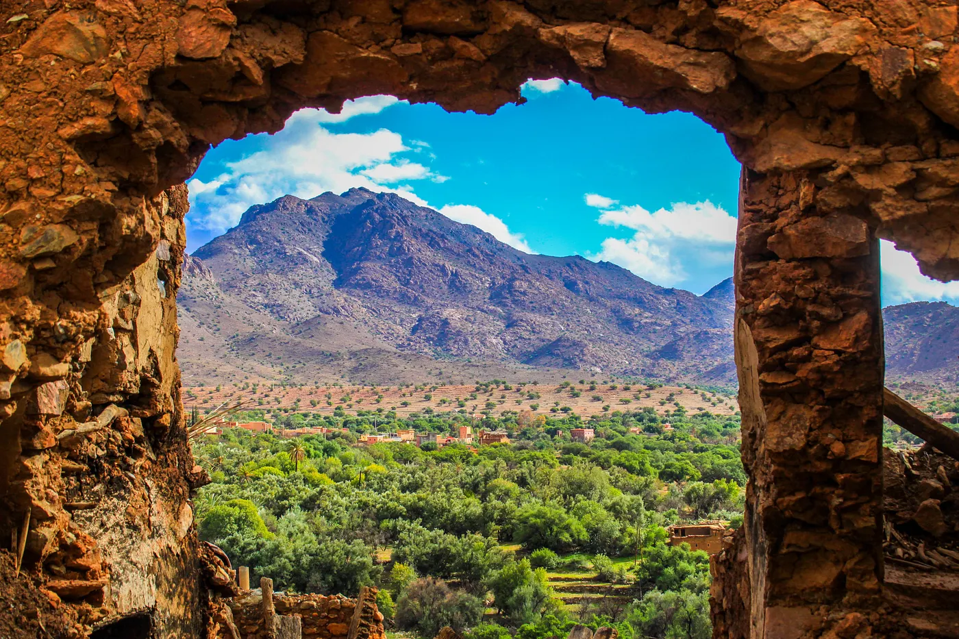 A green valley and mountain range framed by a broken stone arch in Tafraout, Morocco